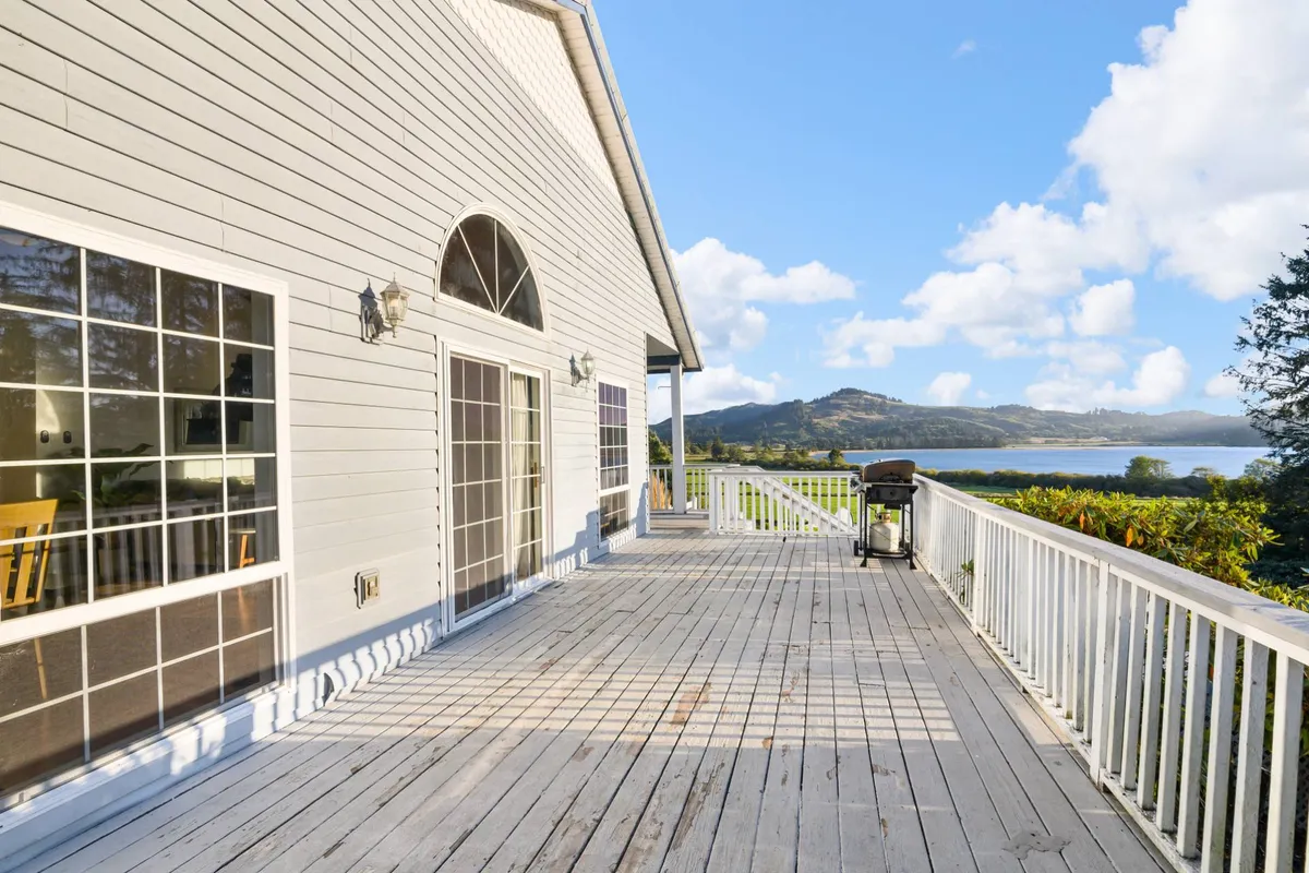 A spacious deck with a grill and large windows overlooking the natural landscape. The scene is set for outdoor dining or socializing, with plenty of room for groups, and the tranquil surroundings hint at scenic sunset views and shared meals.
