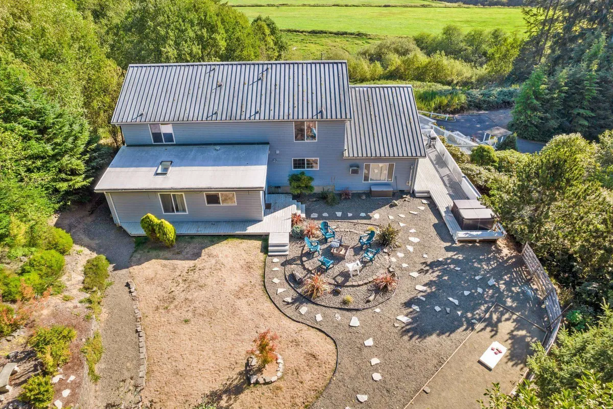 A welcoming exterior view of The Swell House, with the house structure in focus, surrounded by greenery and a well-kept garden path. Outdoor seating areas invite guests to gather, and the warm light suggests it’s either sunrise or sunset, evoking a tranquil, coastal ambiance.