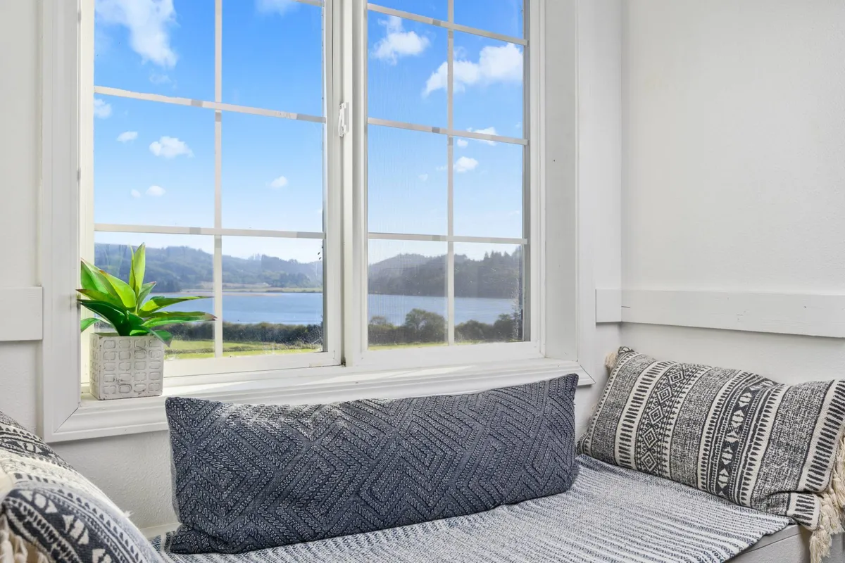A quiet, cushioned window nook framed by a large window with a view, accented by a potted plant. The space is inviting for reading, relaxing, or enjoying peaceful moments alone.