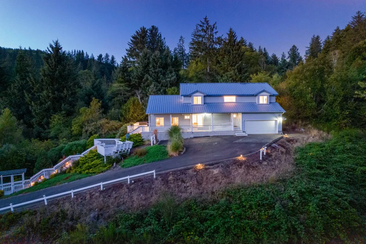 A peaceful exterior view of the house nestled among trees, with a clear pathway leading toward the front entrance. The deck beckons as a spot for evening gatherings, sunset watching, and post-adventure relaxation.