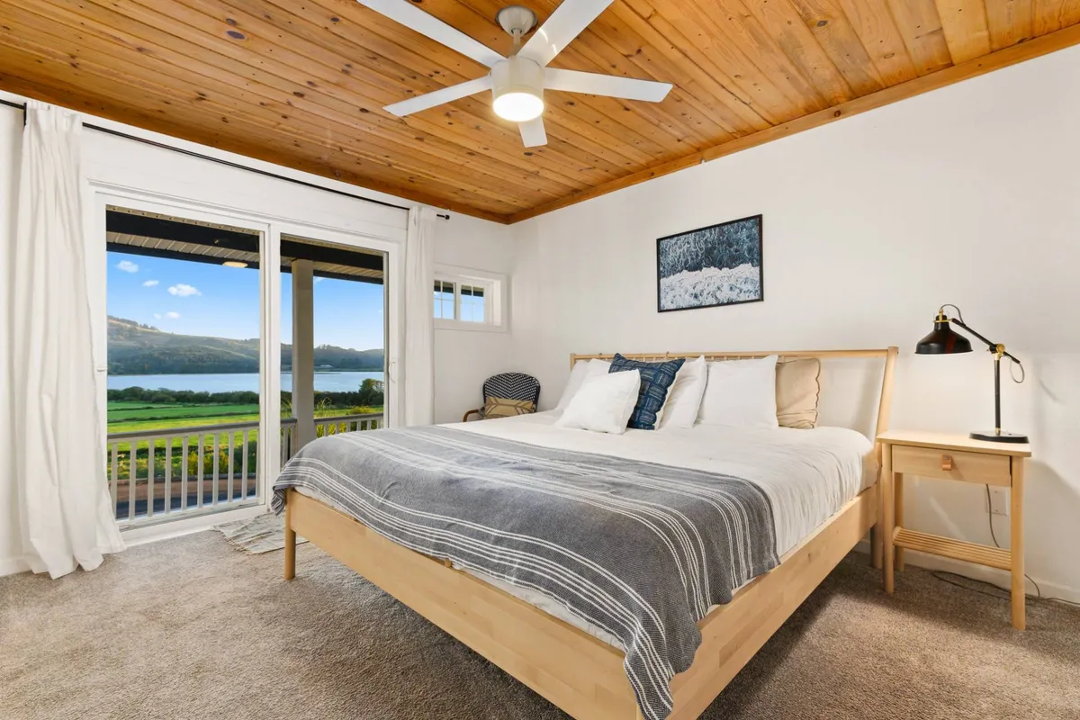 A spacious bedroom featuring a plush bed positioned near a window offering scenic views. The décor includes tasteful artwork and a nightstand, creating a relaxed and inviting atmosphere ideal for rest or reading.