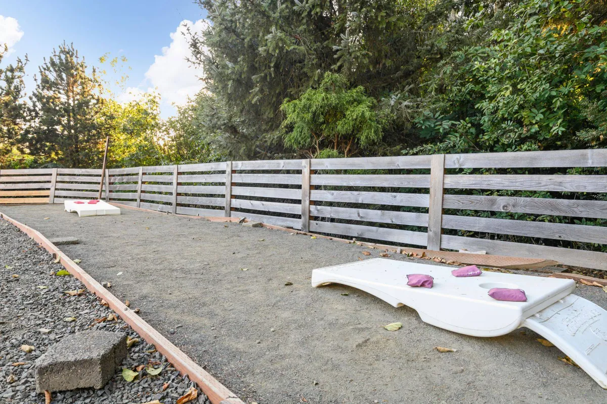 A playful sand area framed by a wooden fence and surrounded by greenery, designed for outdoor games and gatherings. The scene evokes a sense of fun and community, perfect for bocce ball or lawn games like cornhole.