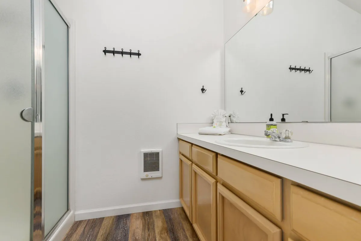 A modern en-suite bathroom featuring a vanity with sink, a large mirror, and a shower area, all illuminated by natural light. The space feels fresh and tranquil, ideal for personal routines or relaxation.