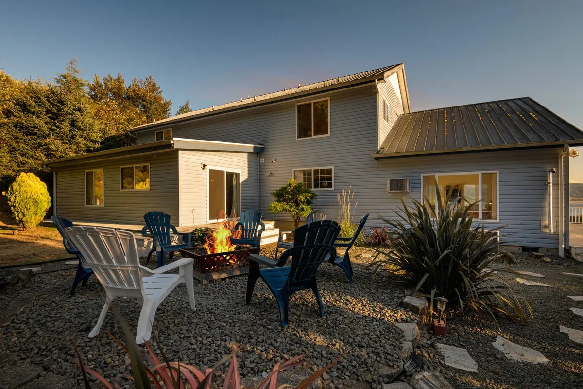 A cozy fire pit area in the backyard, complete with Adirondack chairs, inviting landscaping, and the house in the background. The scene is set for evenings of storytelling, s'mores, and stargazing in a communal and welcoming atmosphere.